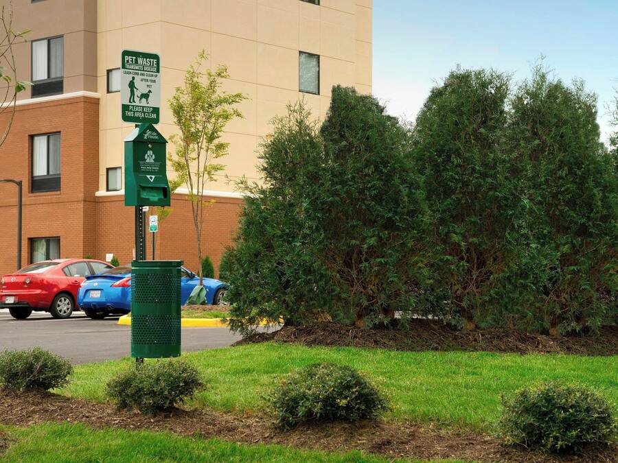 A pet waste disposal sign near a building with a parking lot.