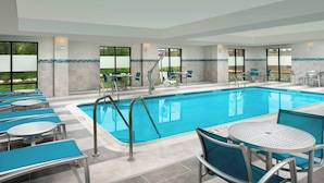 A swimming pool area with lounge chairs and tables, a pool ladder, and large windows offering views of the outdoors. - TownePlace Suites by Marriott Alexandria Fort Belvoir (Alexandria)