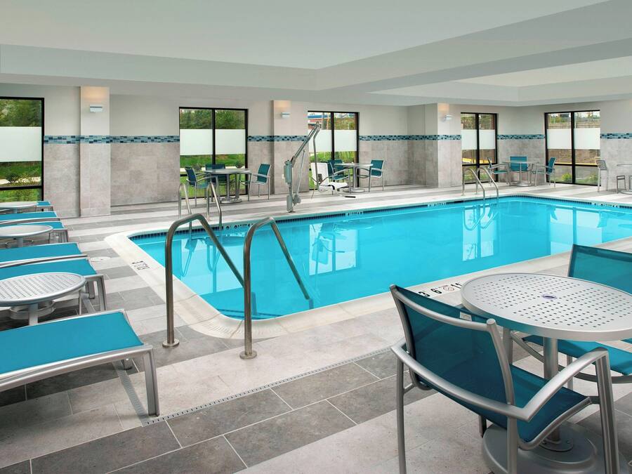 Zona de piscina con sillones reclinables y mesas, una escalera de acceso a la piscina y grandes ventanales con vistas al exterior.