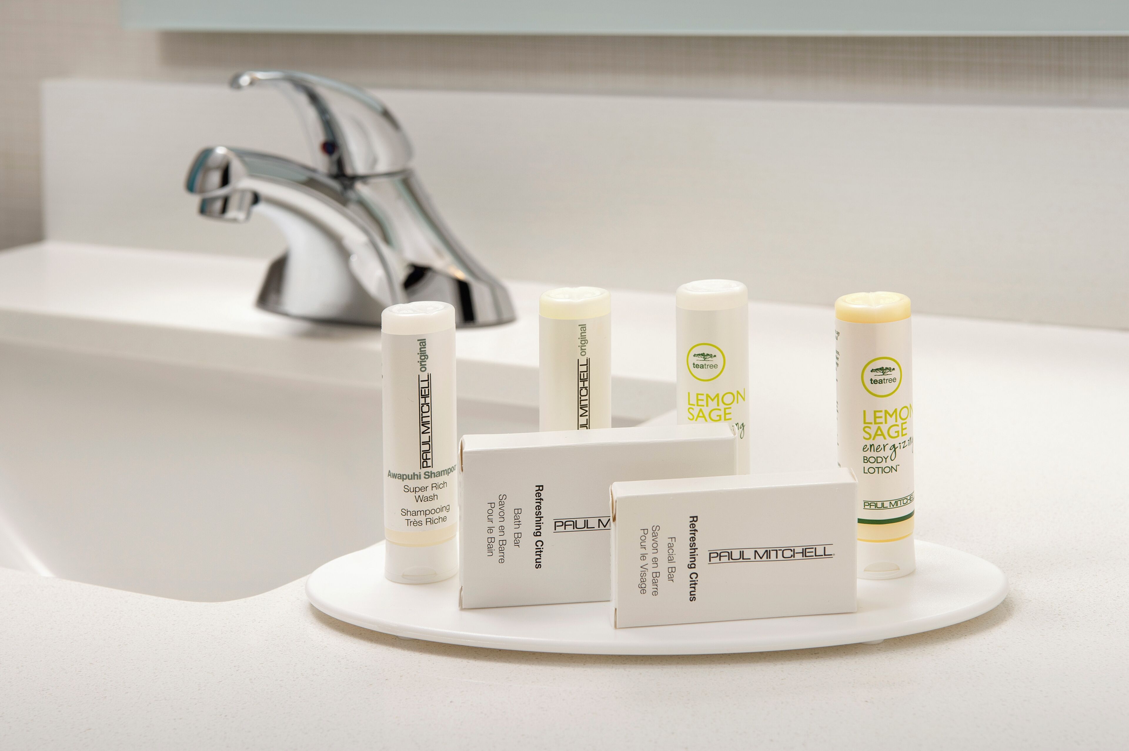 A bathroom sink with a modern faucet, a tray holding various Paul Mitchell hair care products, and a white countertop.