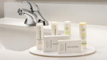 Un lavabo de salle de bain doté d’un robinet moderne, un plateau contenant divers produits de soins capillaires de la marque Paul Mitchell et un comptoir blanc.