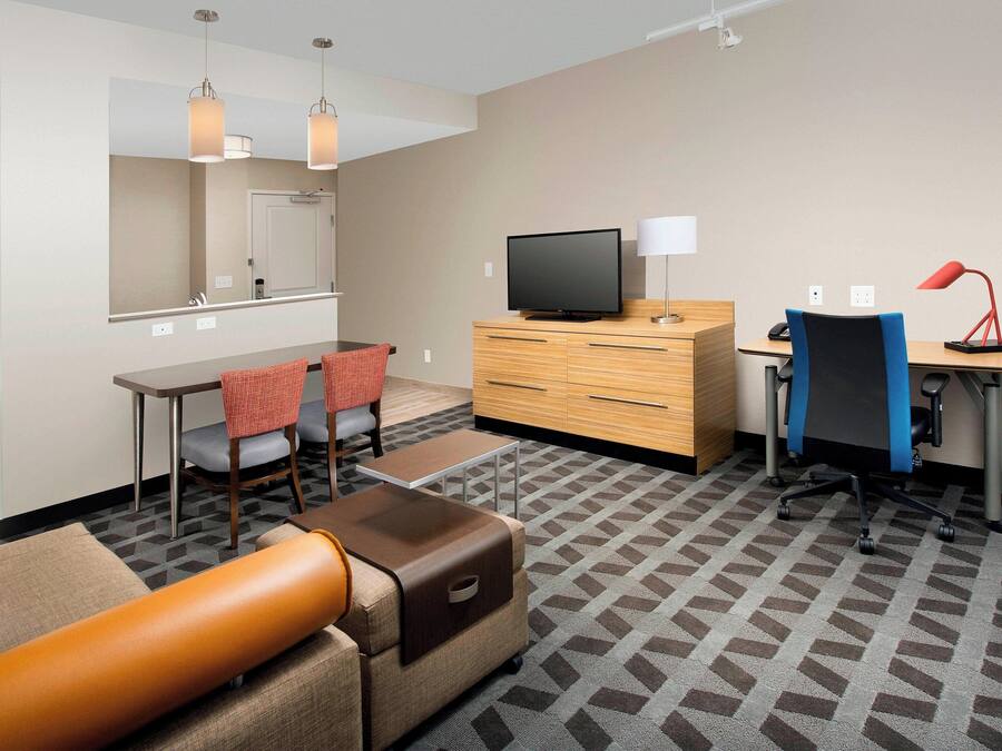 Ein Hotelzimmer mit einer Couch, einem Fernseher, einem Schreibtisch mit Lampe, einem Sessel und einem Spiegel.