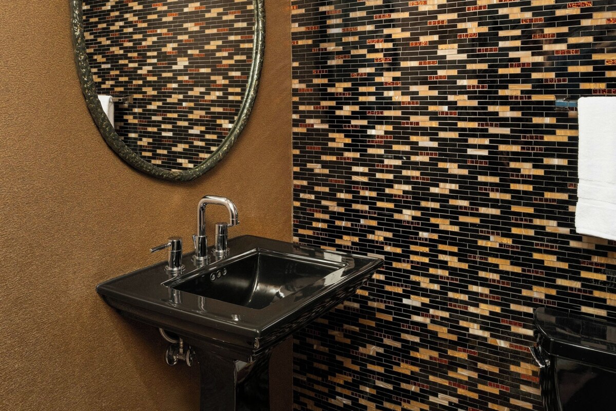 Un baño con un lavamanos negro, un espejo redondo y una pared con diseño.