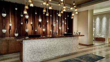 A reception area with a wooden panel wall, hanging pendant lights, a marble counter, and a textured wall in the background.