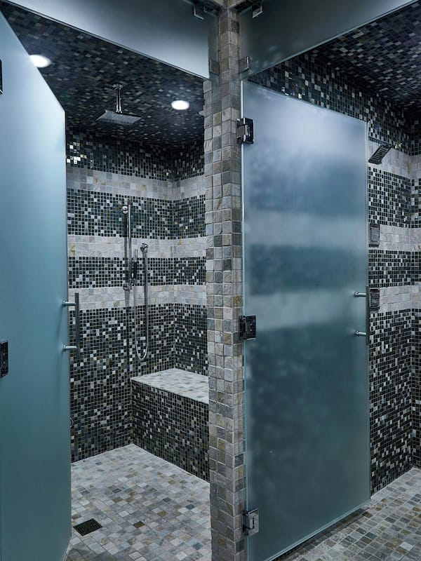 Bathroom features a mosaic tile design, a large glass door, and a shower area with handheld showerhead and wall-mounted faucet.