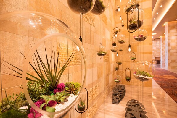 Un interior moderno con una gran jardinera circular llena de plantas y flores, rodeada de esferas de vidrio colgantes con follaje.