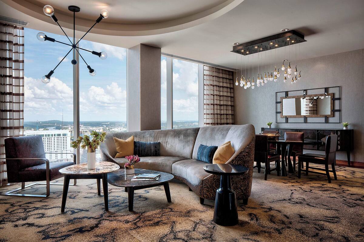 A modern living room with a large sofa, a coffee table, and a dining area with a chandelier.