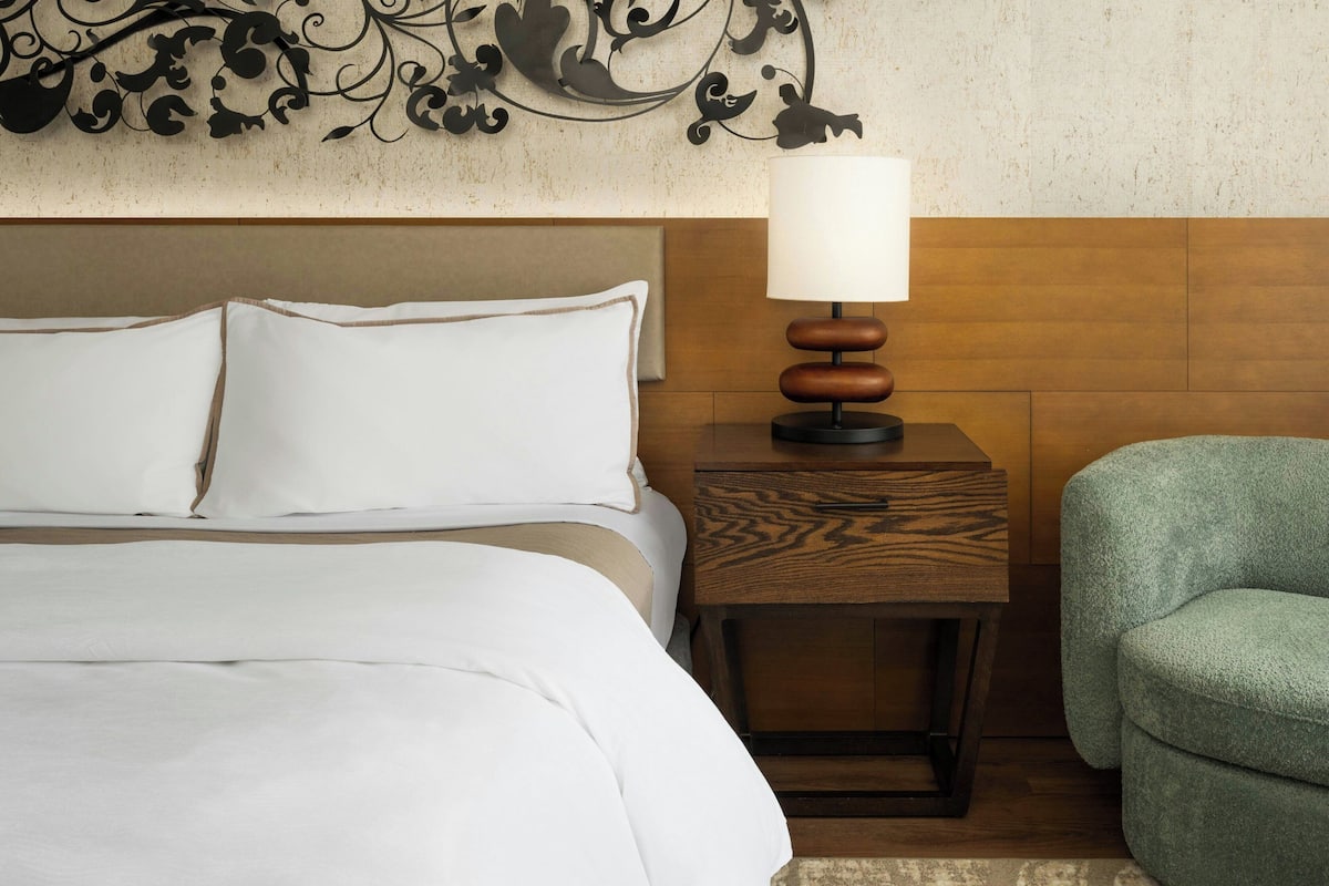 A hotel room with a bed, a nightstand with a lamp, and a green armchair.