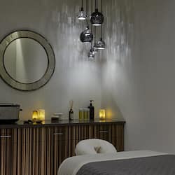Relax in a serene space with a large round mirror, bedside table, and comfortable bed.