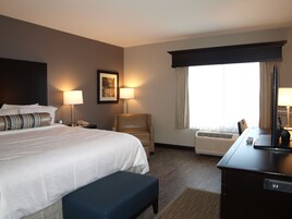 Una habitación de hotel con una cama grande, lámparas de noche, un escritorio con una computadora, una silla y un ventanal con cortinas.