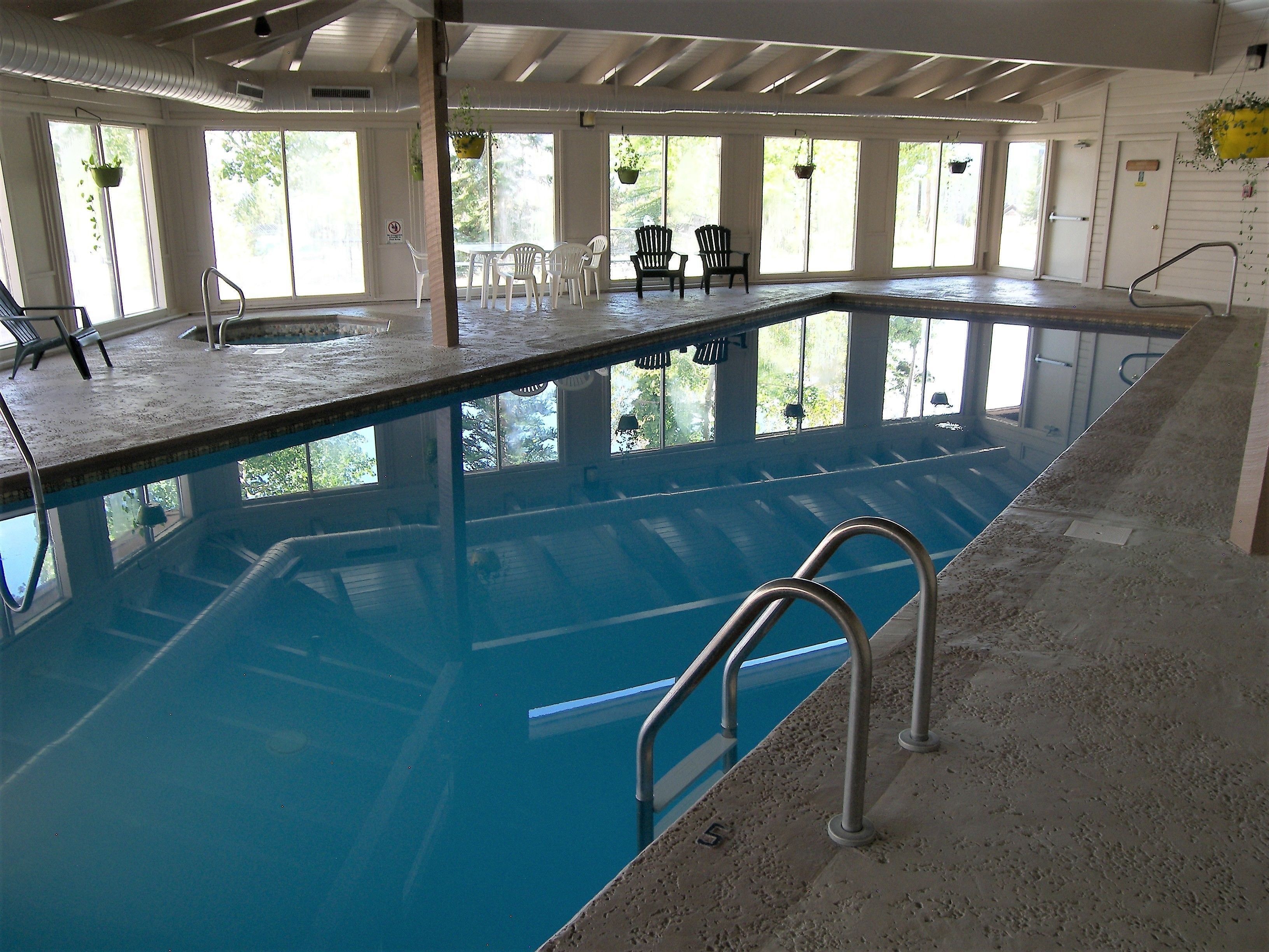Piscina interior con agua cristalina, rodeada de ventanas y sillas.