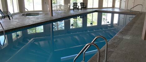 Piscina interior con agua cristalina, rodeada de ventanas y sillas.