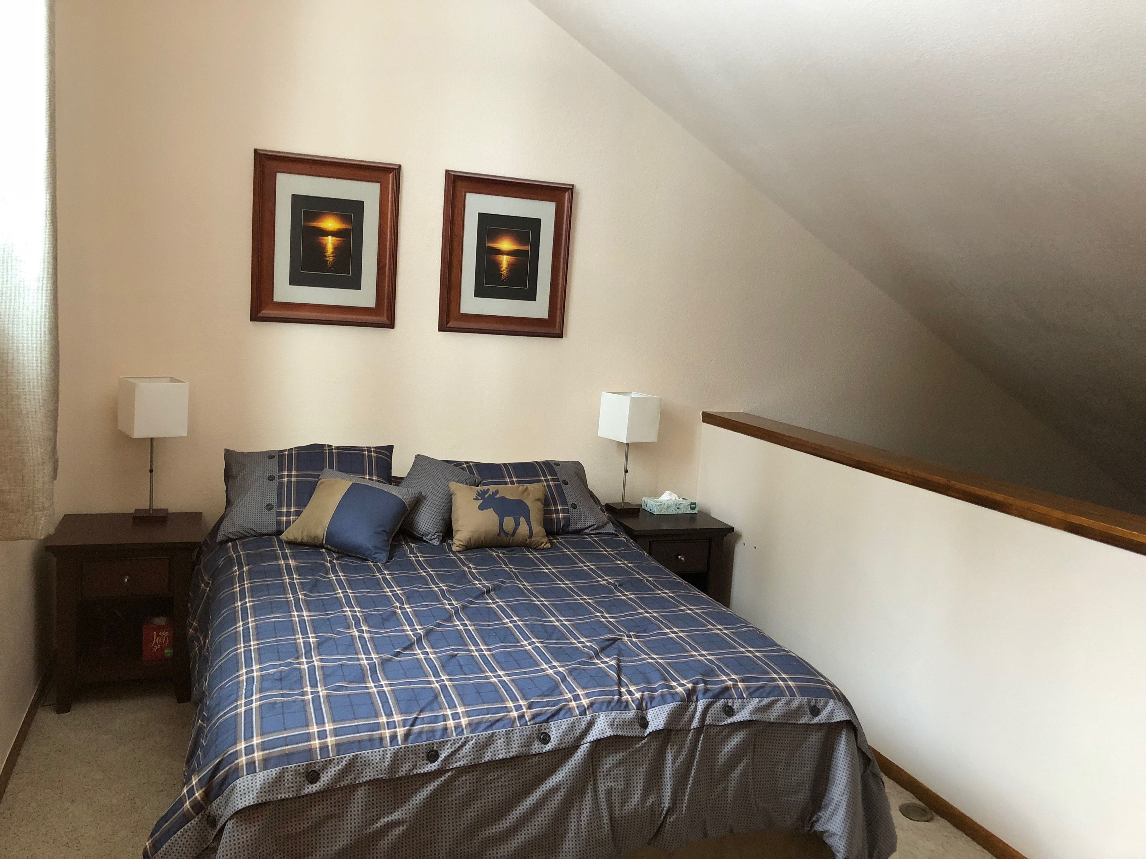 A bedroom with a bed, two nightstands, two wall-mounted lamps, and two framed pictures.