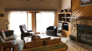 A cozy living room with a fireplace, a sofa, a chair, and a television. - Buffalo Ridge 2 Bed Loft (Silverthorne)
