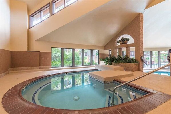 An indoor swimming pool with a tiled edge, a wooden deck, and a stone wall. - 3106 Champagne Lodge, Trappeur's Crossing Apartment 2 SimplySteamboat (Steamboat Springs)