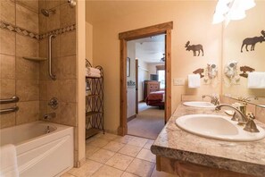 A bathroom with a bathtub, a shower with a handrail, and a vanity with two sinks and a mirror. - 3106 Champagne Lodge, Trappeur's Crossing Apartment 2 SimplySteamboat (Steamboat Springs)