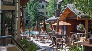 Ein Außenbereich mit Terrasse, Tischen, Stühlen, einem Pool und einem Holzgebäude mit Schornstein.