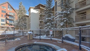 Une zone avec piscine, délimitée par une clôture, des arbres couverts de neige et, au loin, des immeubles à plusieurs étages.