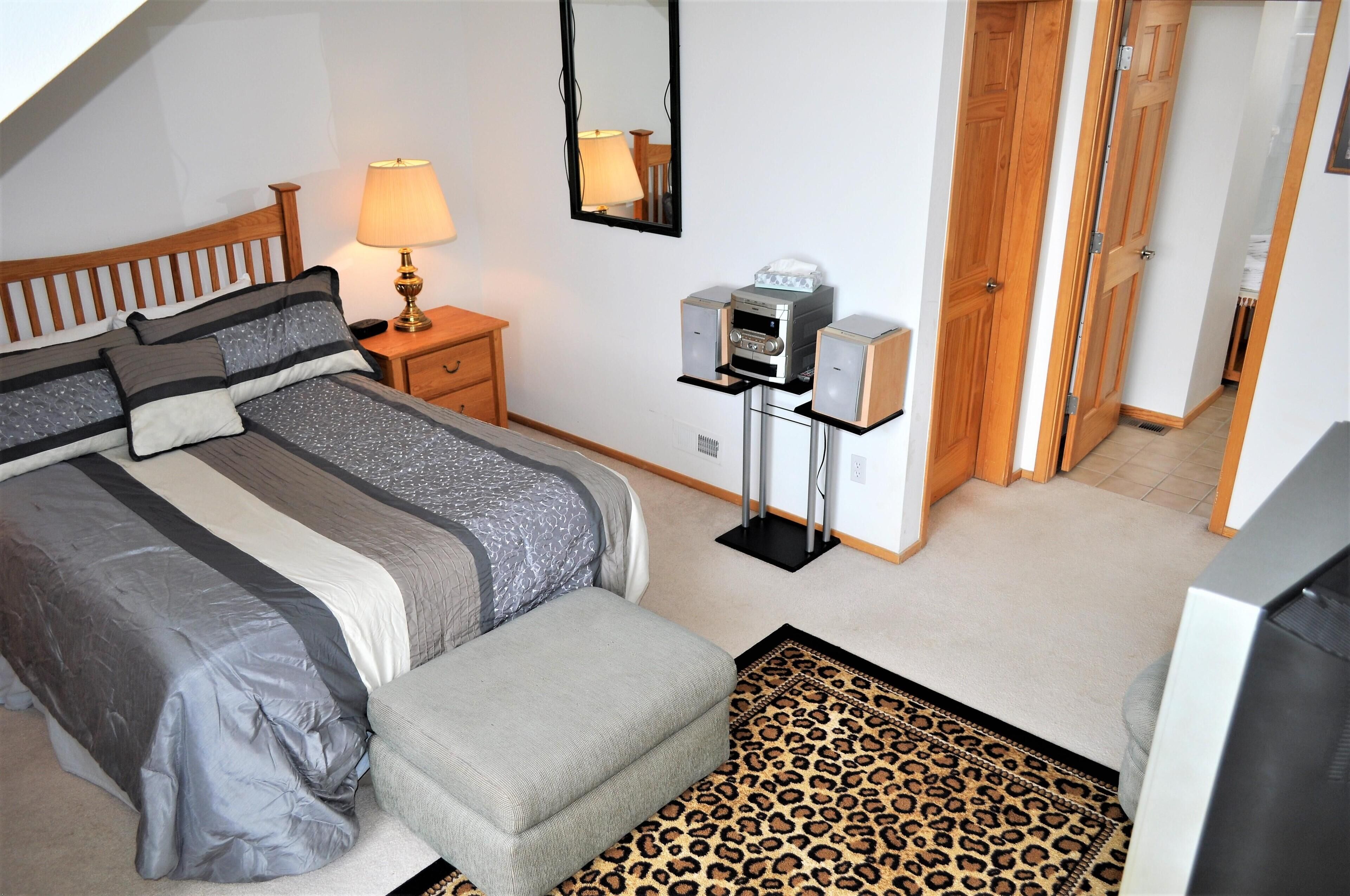 A bedroom with a bed, bedside table, lamp, speakers, and a wardrobe.