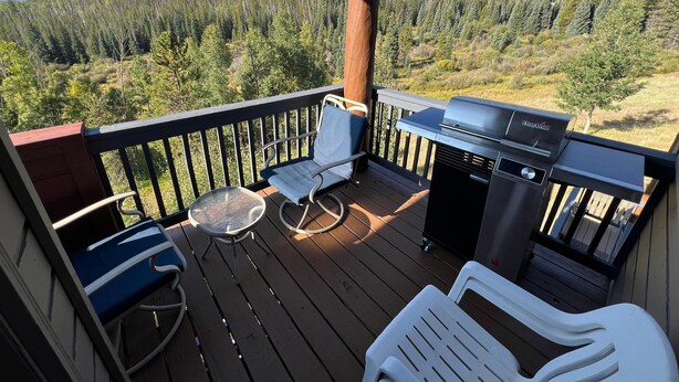 A deck with a grill, chairs, and a table overlooking a forested mountain range.
