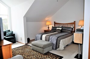A bedroom with a bed, two bedside lamps, a wooden headboard, a grey ottoman, a leopard print rug, and a window with a view of trees. - Forest Park 3 Bed 4 Bath Townhome (Silverthorne)