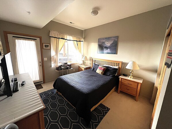A hotel room with a bed, bedside tables, a desk with a computer, a window with curtains, and a painting on the wall. - Forest Park 3 Bed 4 Bath Townhome (Silverthorne)