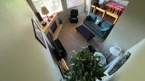 A living room with a sofa, coffee table, and a fireplace. There is a window with blinds, a lamp, and a plant.