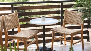 A balcony with two wicker chairs and a small table, overlooking a lush green landscape. - The Frances Modern Inn (Austin)