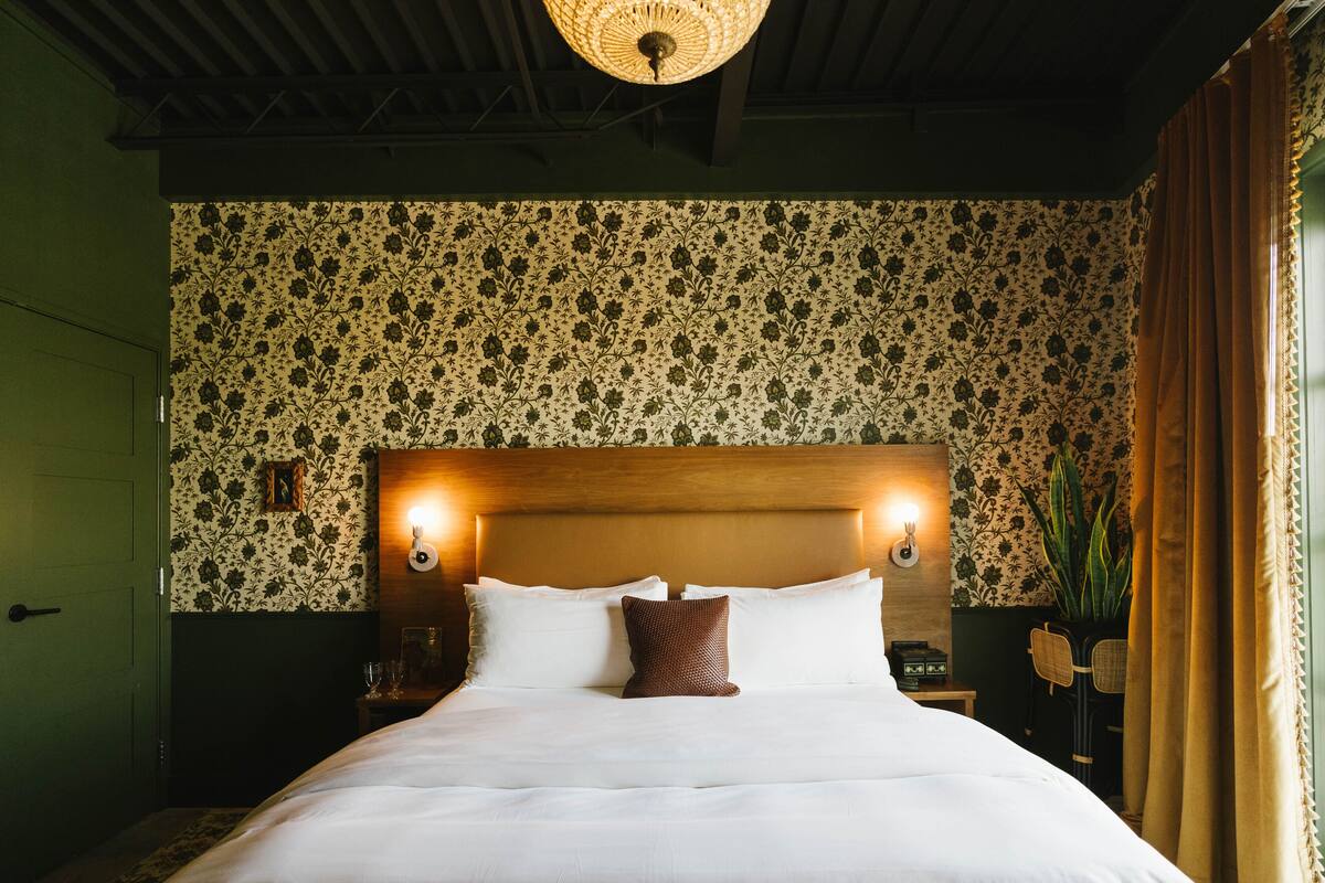 A neatly made bed with white linens, a wooden headboard, and two wall-mounted reading lamps.