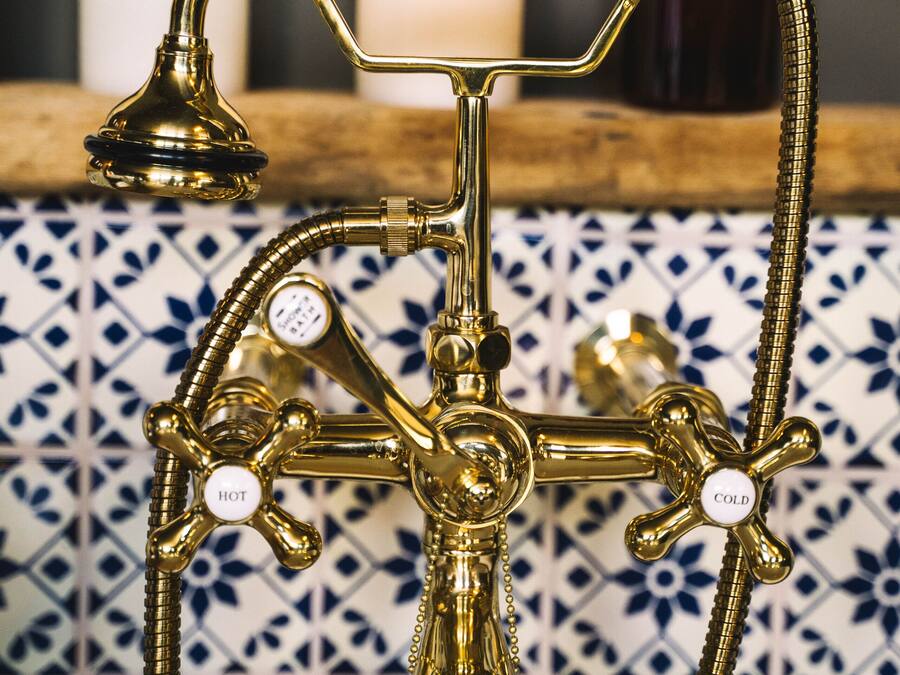 Un accesorio de baño de bronce con un mando blanco, caño de agua fría y caliente, y cabezal de ducha.