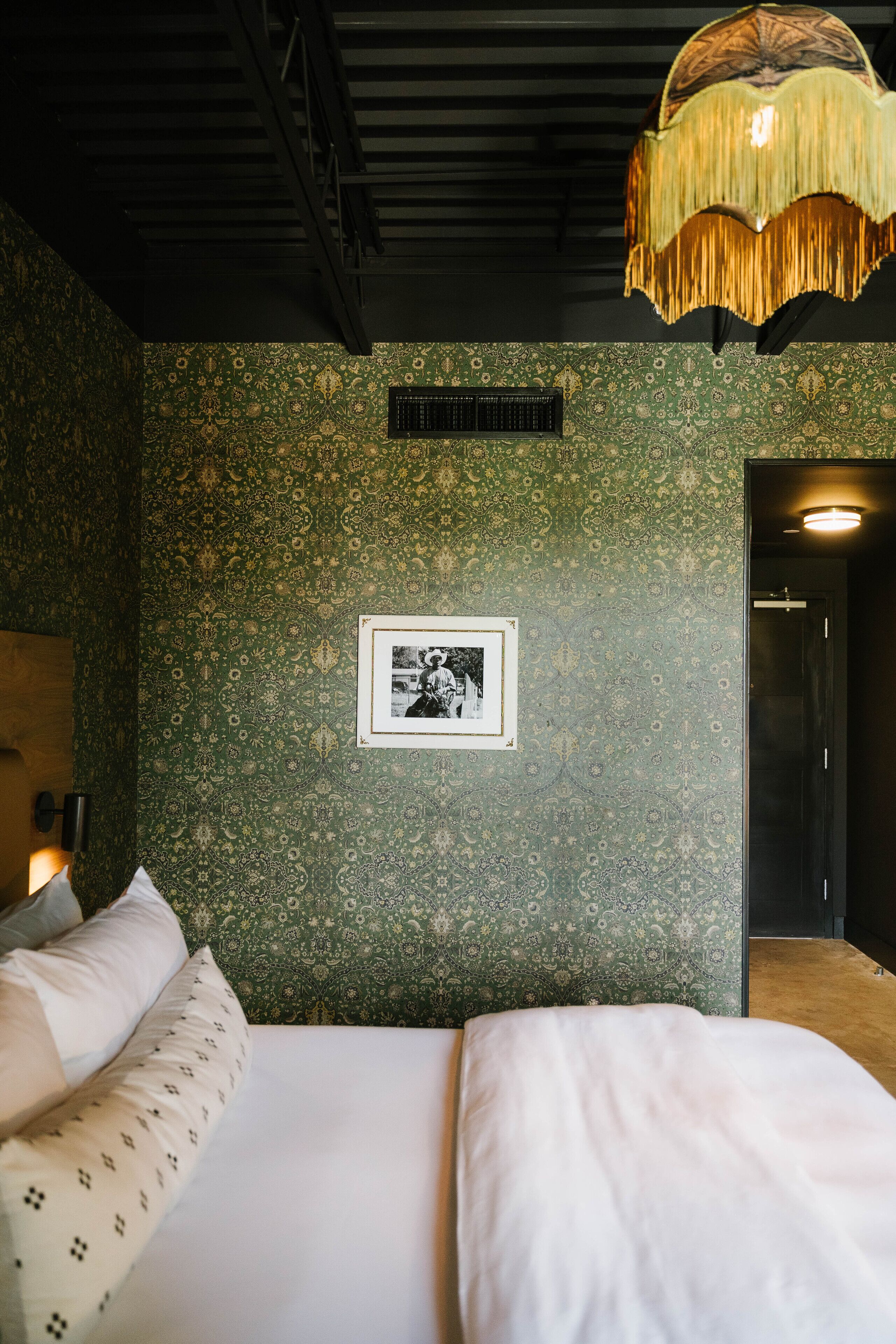 A room with a bed, a framed picture on the wall, and a hanging light fixture.