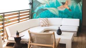 A modern living room with a white sofa, a woven chair, and a small table with a cactus. A large tropical mural decorates the wall. - The Frances Modern Inn (Austin)