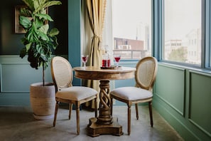 Een ronde houten tafel met twee gestoffeerde stoelen, een potplant en twee glazen rode drank op tafel.