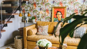 A living room with a staircase, a sofa, a coffee table, and a patterned wallpaper. - The Frances Modern Inn (Austin)