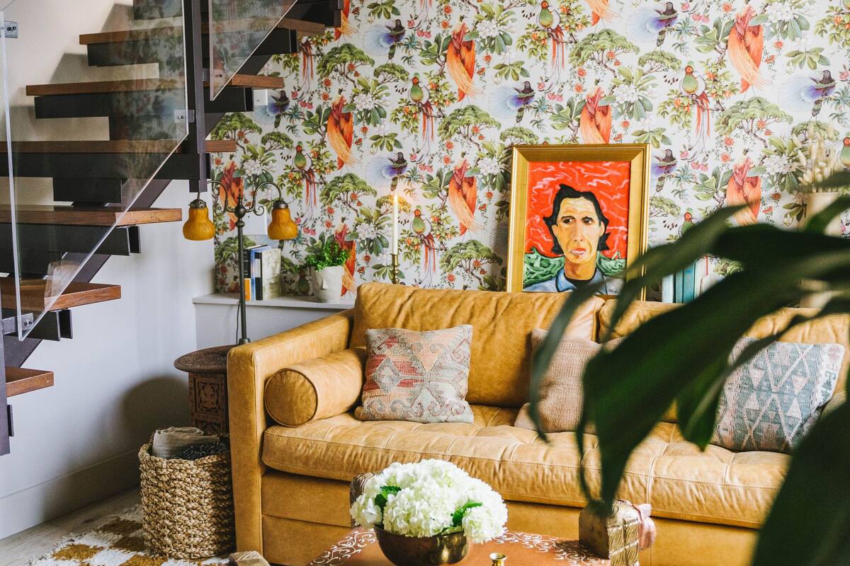 A living room with a staircase, a sofa, a coffee table, and a patterned wallpaper.