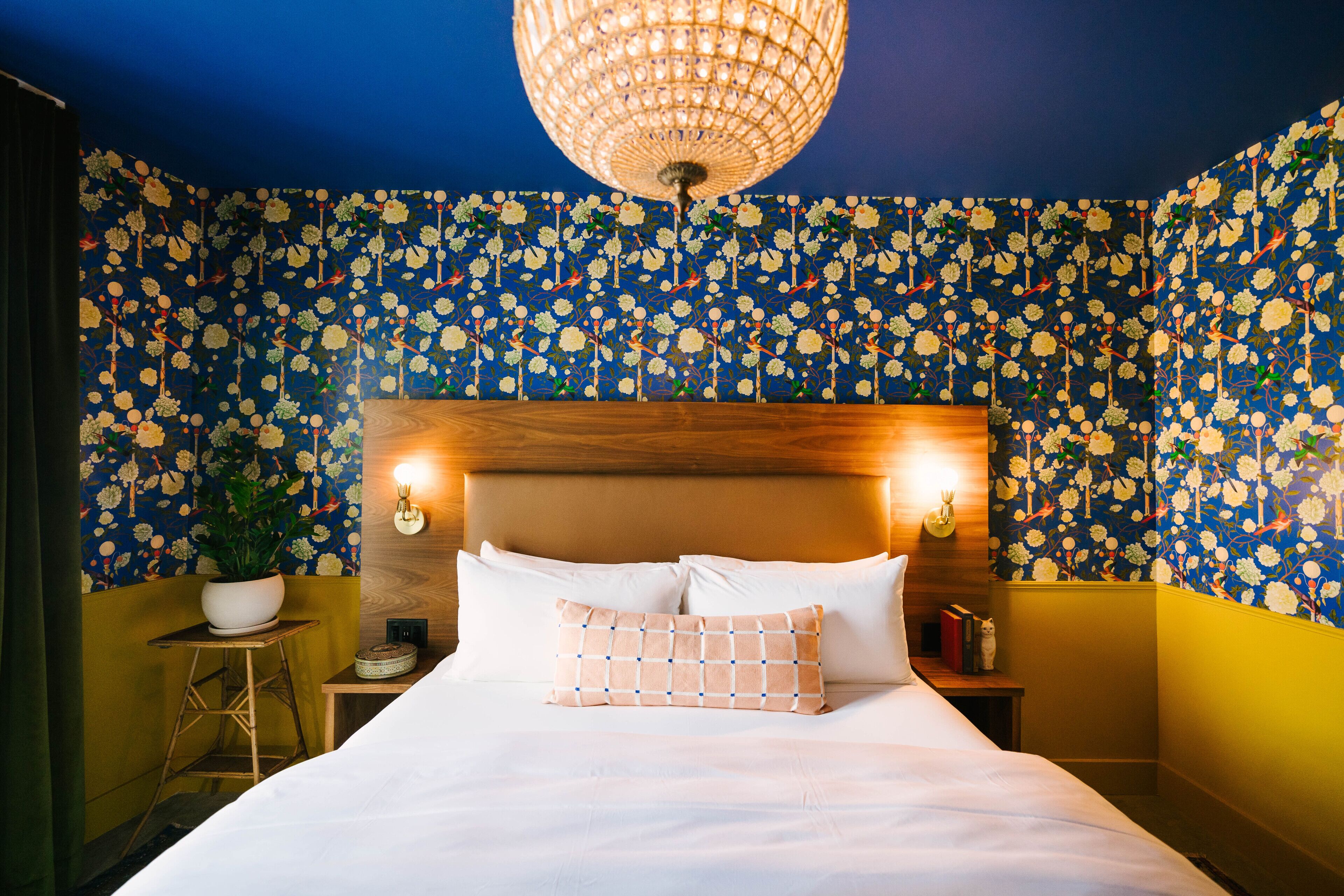 A bedroom with a floral wallpaper, a wooden headboard, a white bed, and a hanging light fixture.