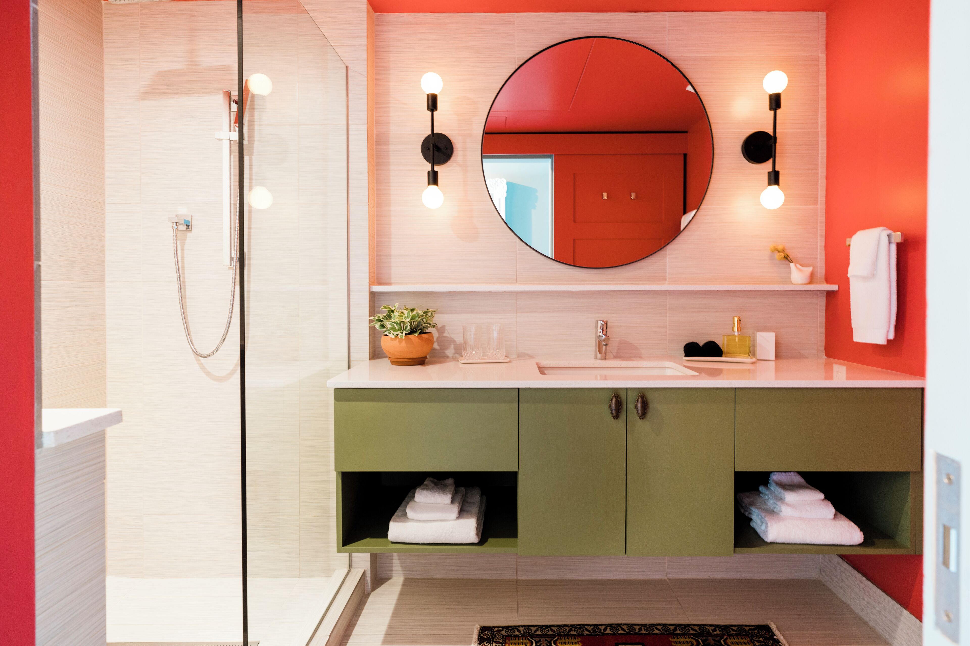 A modern bathroom with a glass shower enclosure, a large mirror, and green cabinets.