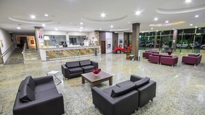 A hotel lobby with a reception desk, seating area, and a glass entrance to the parking area. - Hotel Golden Park Sorocaba & Convenções - by Nacional Inn (Sorocaba)