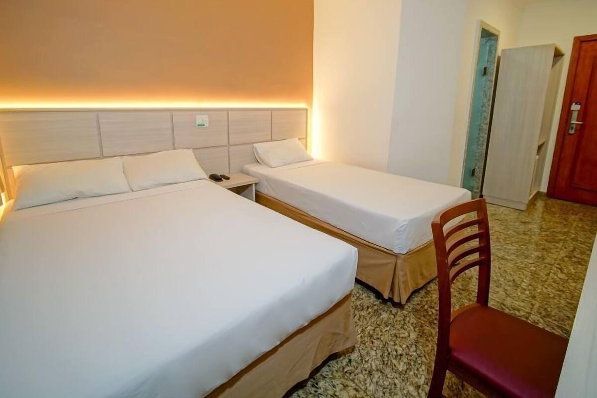 A hotel room with two single beds, a wooden chair, and a small table.