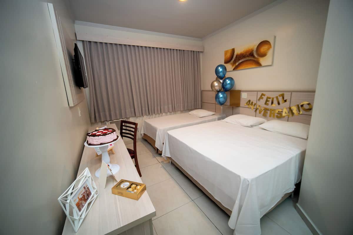 A hotel room with two single beds, a desk with a cake, and a 'Feliz Aniversario' decoration.