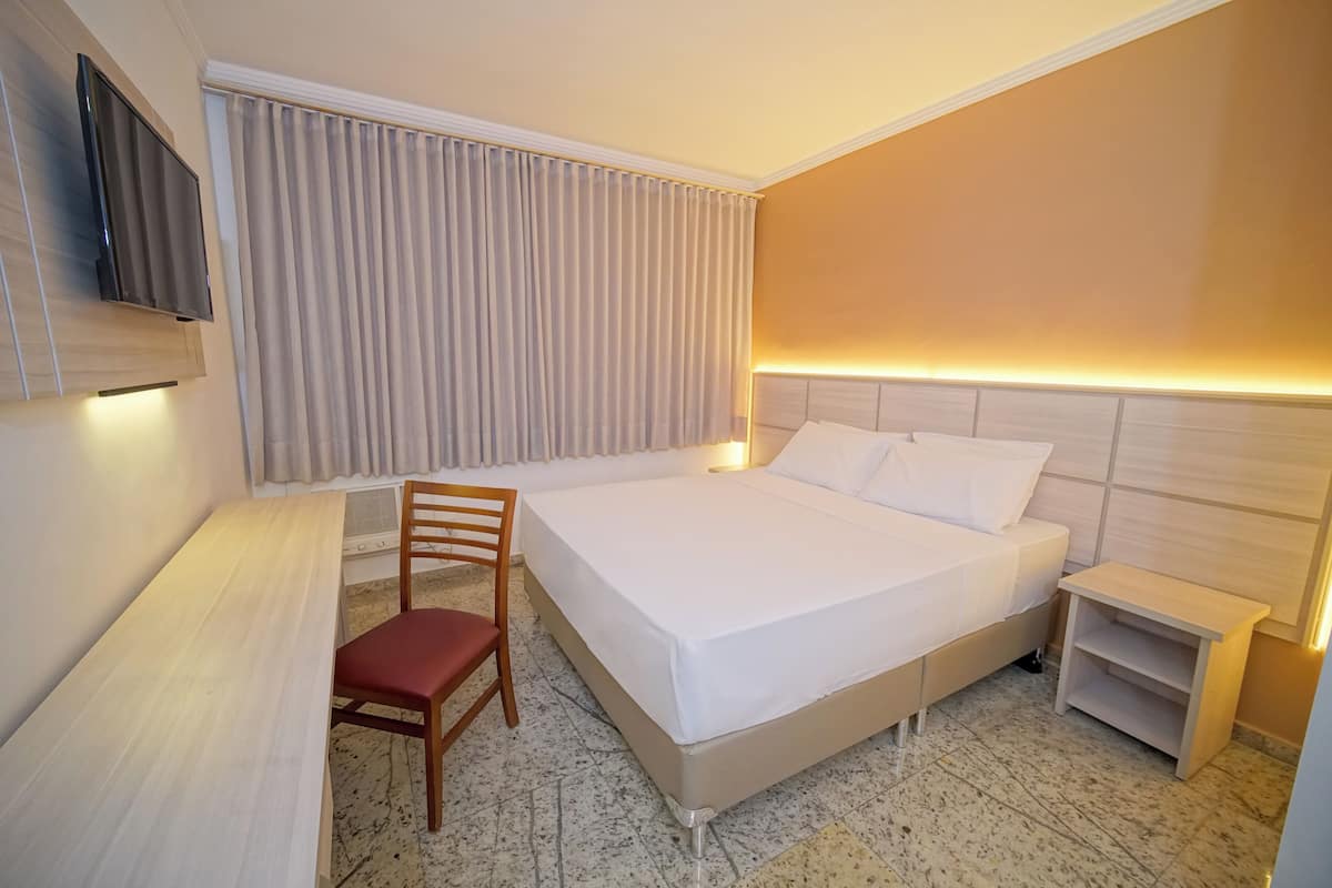 A hotel room with a bed, a desk, a chair, a TV, and a nightstand.