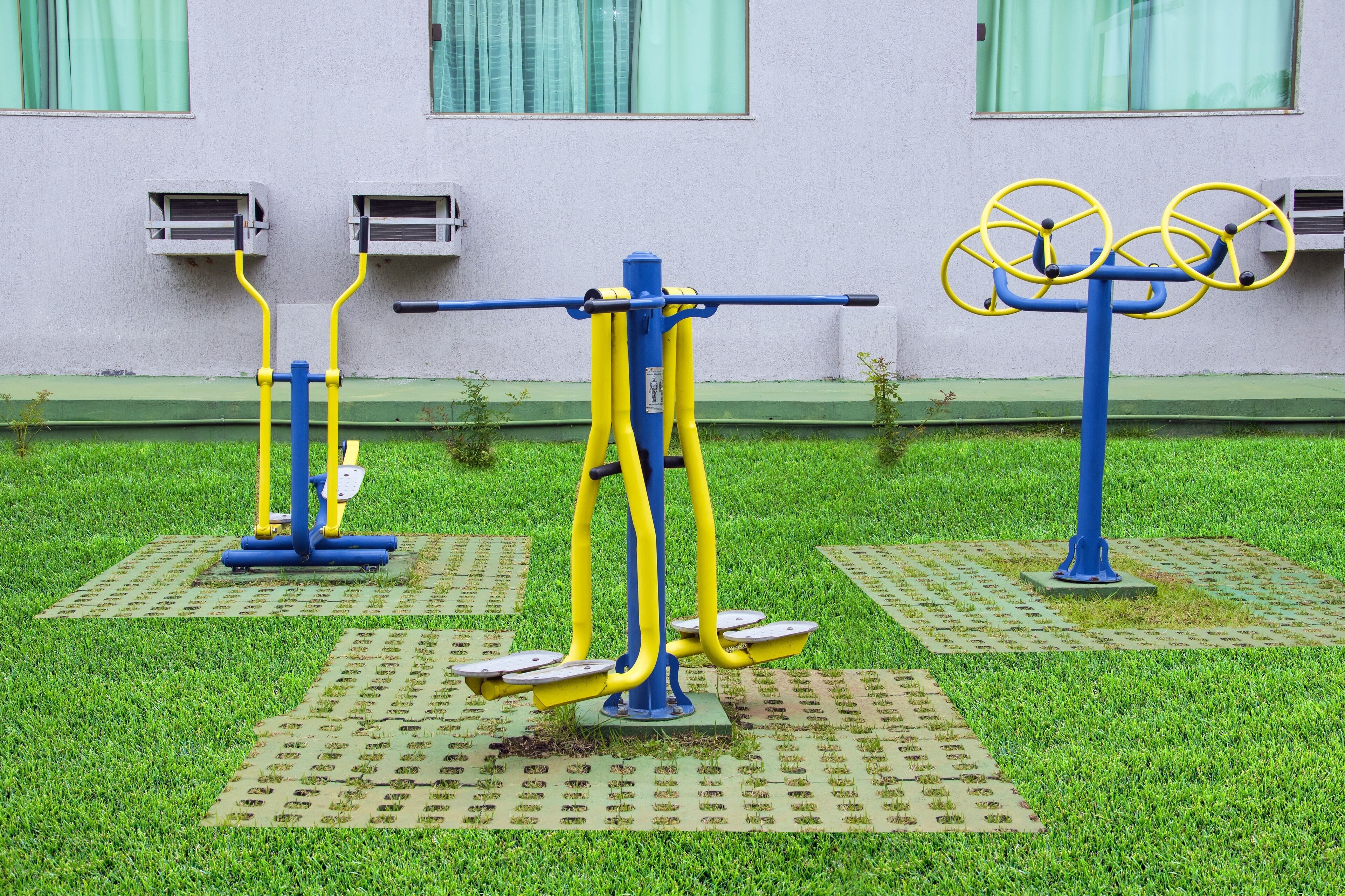 Equipamentos de exercícios ao ar livre em uma área gramada, com um edifício ao fundo.