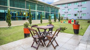 An outdoor patio with a wooden table and chairs, surrounded by potted plants and a playground in the background. - Hotel Golden Park Sorocaba & Convenções - by Nacional Inn (Sorocaba)