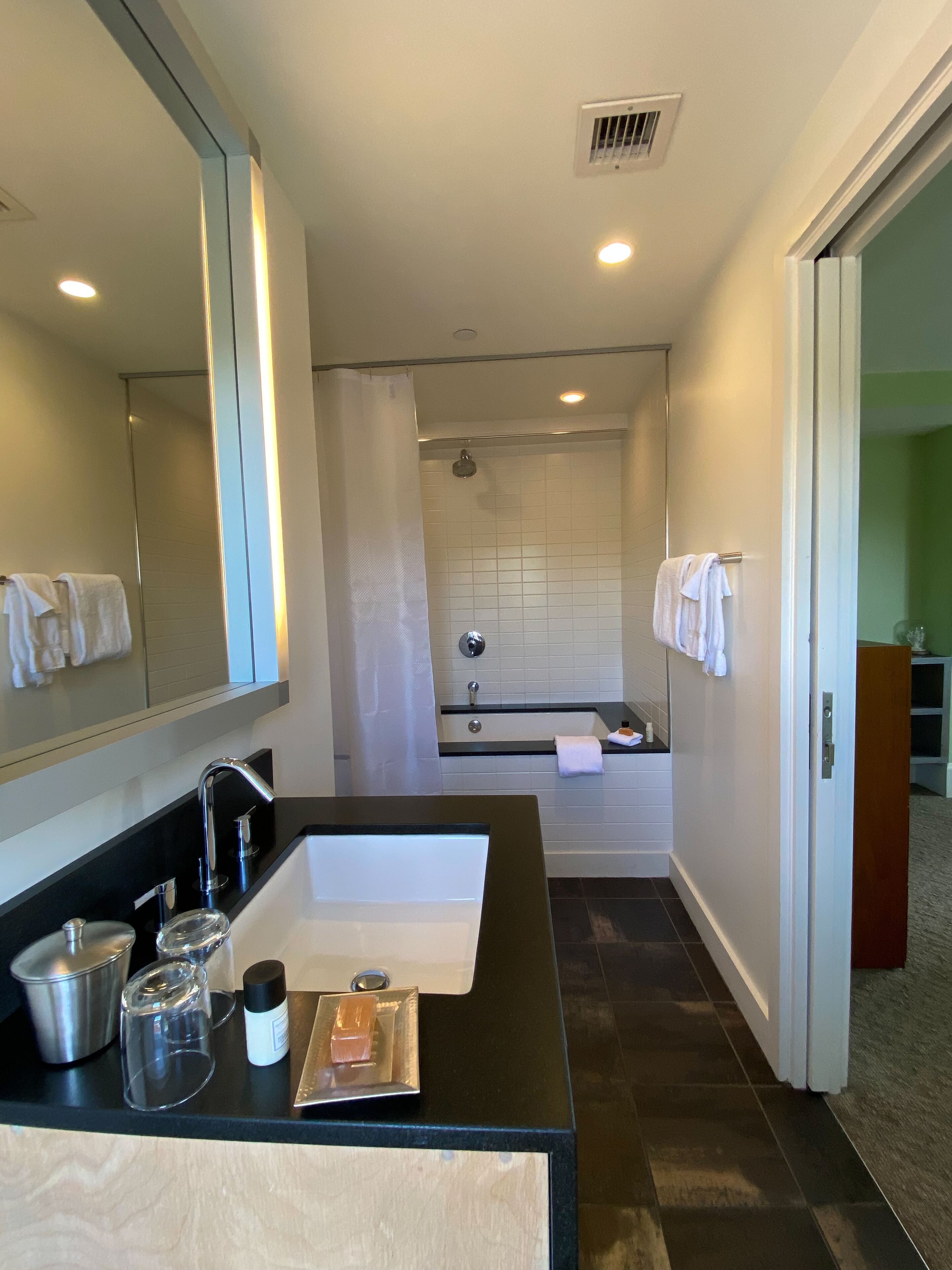 Une salle de bain moderne avec un lavabo sur un plan de toilette noir, un grand miroir et un espace douche.