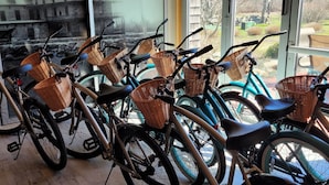 Bicycles with baskets parked indoors, a wooden floor, and a view of trees through large windows. - Stone House Inn (Little Compton)