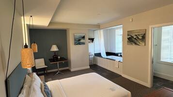 A modern hotel room with a large bed, a desk, a chair, and a view of the outside through a sliding door.