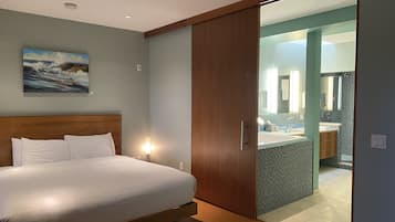 A bedroom with a bed, a painting, and a bathroom visible through an open door.