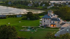 A large stone house with a prominent tower, surrounded by lush green lawns and a view of the sea. - Stone House Inn (Little Compton)