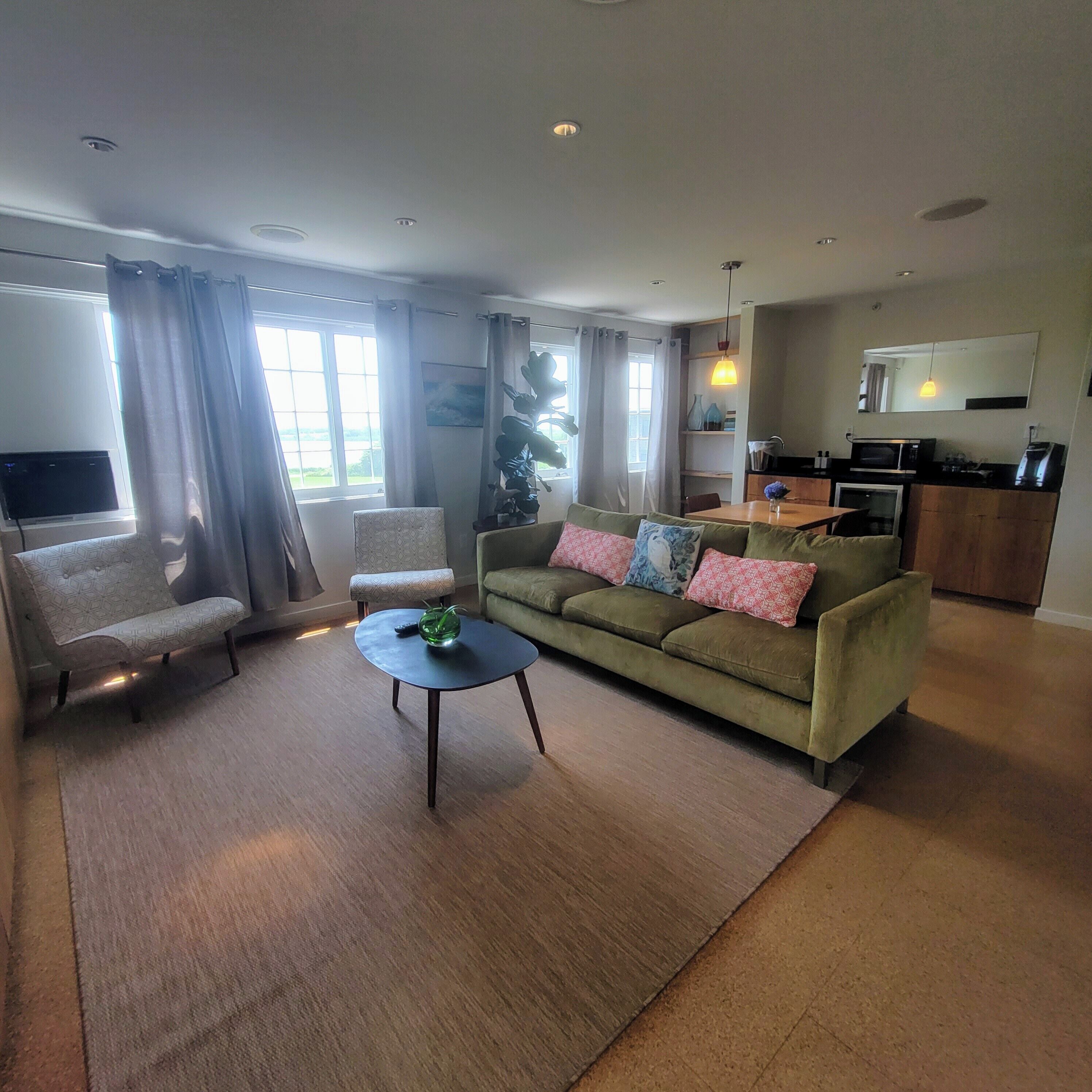 A living room with a sofa, armchairs, a coffee table, and a kitchen area with a microwave and oven.