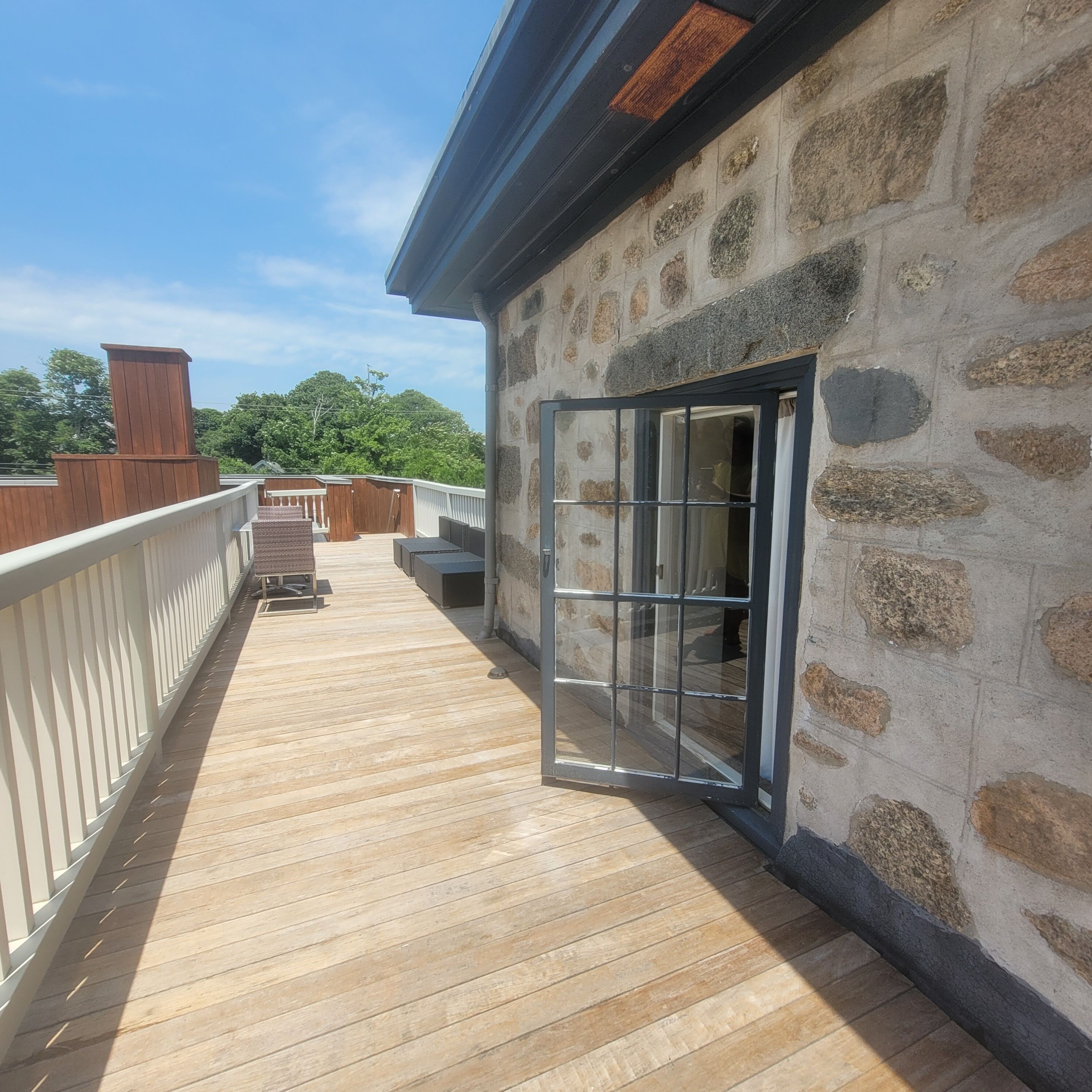 Una terraza de madera con un muro de piedra y un ventanal que da a una habitación.